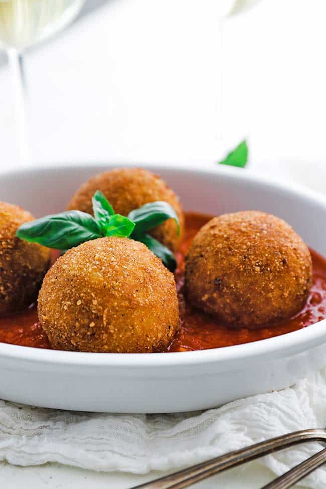 browned risotto arancini in a dish with tomato sauce and basil