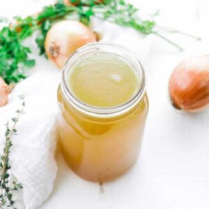 jar of chicken stock next to mirepoix vegeteables