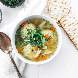 bowl of chicken stoup with matzo balls and fresh herbs