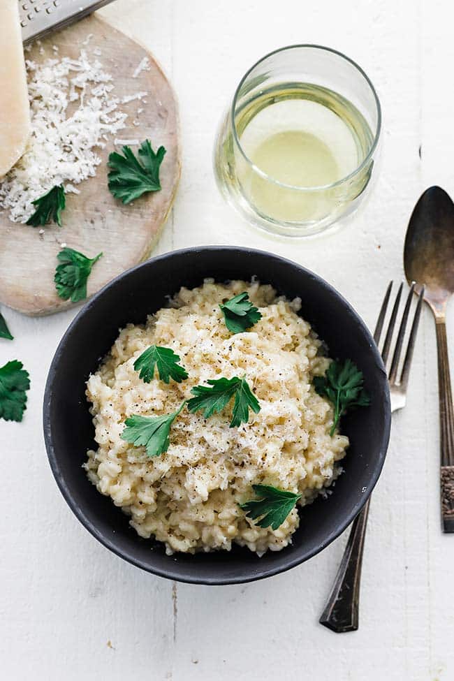 risotto in a bowl with silverware and a glass of white wine