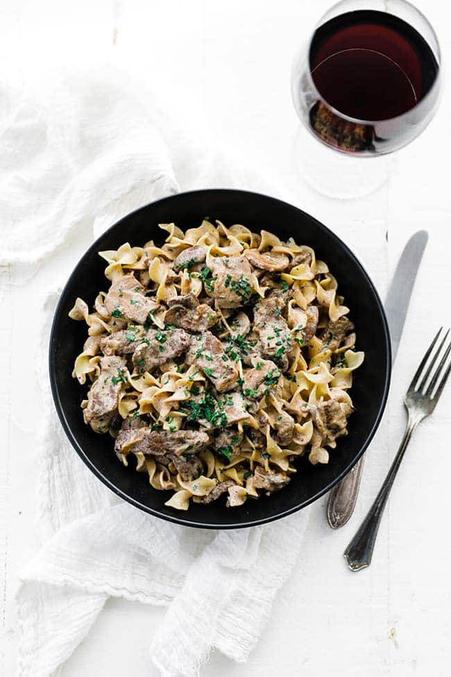 glass of wine with plate of egg noodles, beef and mushrooms
