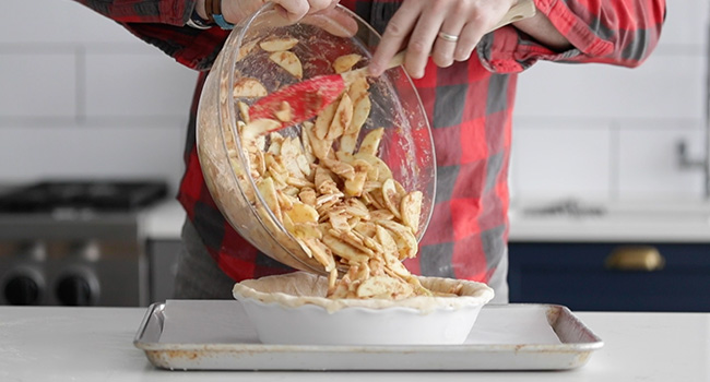 adding apples to pie dough in a pan
