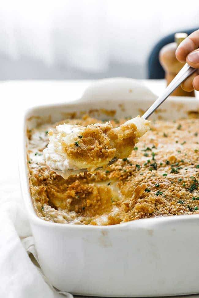 taking a spoonful of potatoes au gratin out of a casserole dish