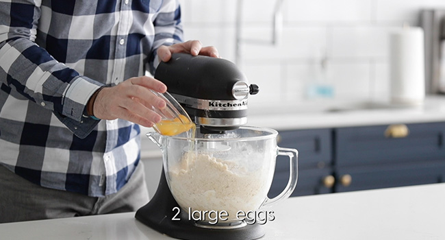 adding eggs to a stand mixer with dough