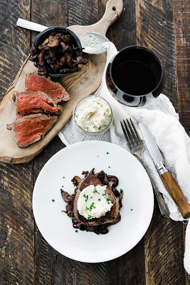 sliced filet mignon on a cutting board and a whole steak on a plate