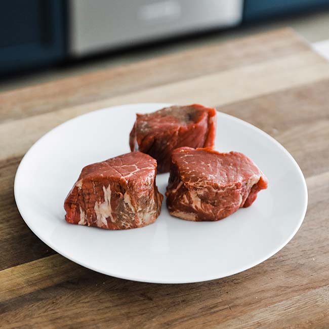 3 individual filet mignon steaks on a plate on a cutting board