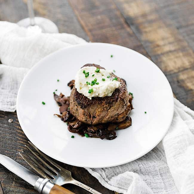 cooked filet mignon on a plate with herb butter on top