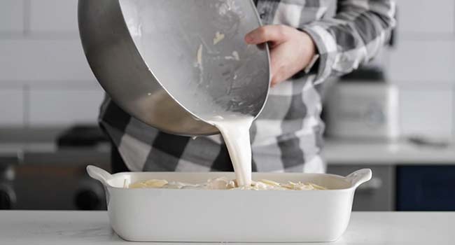 pouring cream on sliced potatoes in a pan