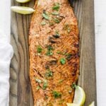 a whole side of cooked salmon with sauce and lemons on a cutting board