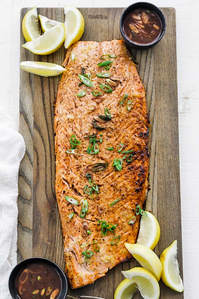 a whole side of cooked salmon with sauce and lemons on a cutting board