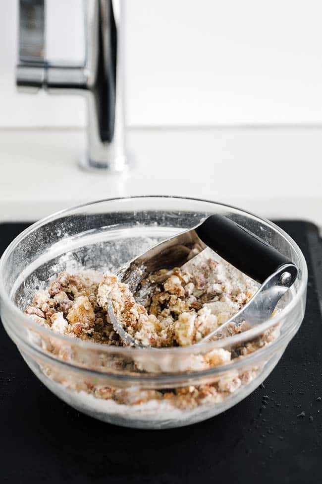 a bowl with a pastry knife cutting in butter with pecans and flour
