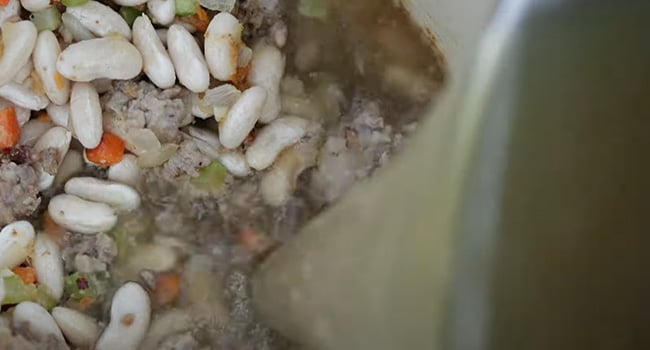 adding stock to a pot with beans