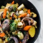 black bowl with roasted carrots, brussel sprouts, potatoes and onions