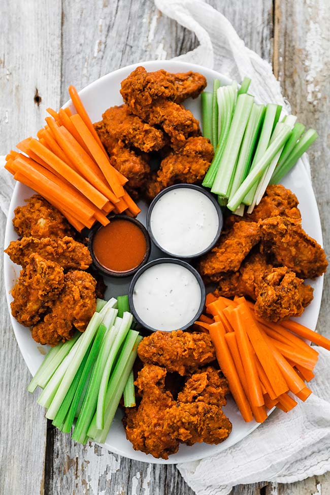 platter of cooked buffalo wings with veggies and sauce