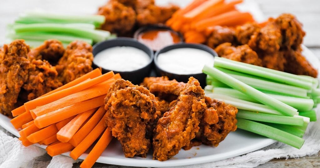 platter of cooked buffalo wings with veggies and sauce