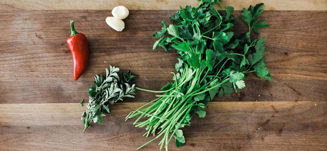 cutting board with parsley, oregano, peppers and garlic