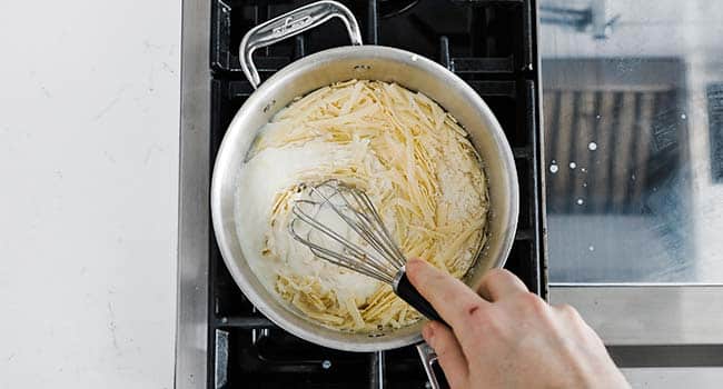 whisking cheese into a pot with bechamel 