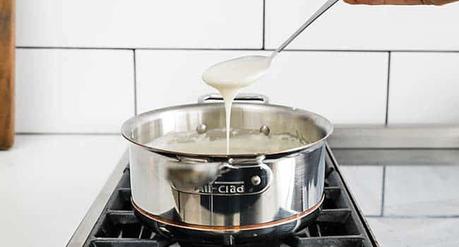 a spoon pouring white sauce into a pot