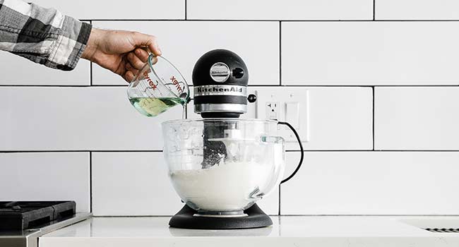 pouring oil into a stand mixer with flour