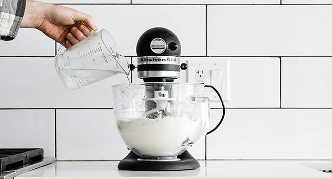 adding water to a stand mixer with flour