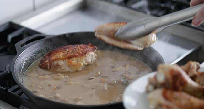 placing chicken into a pan with gravy
