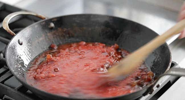 cooking crushed tomatoes in a pan with cooked guanciale
