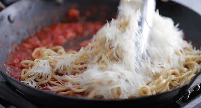 tossing pasta with a tomato sauce and shredded cheese