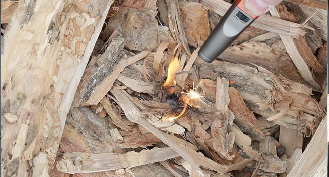 using a lighter to light tinder and kindling