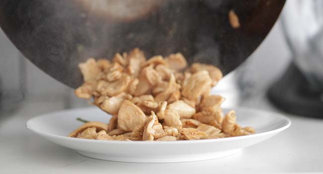 removing cooked chicken from a wok onto a plate