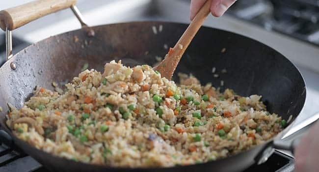 stirring fried rice in a wok with vegetables and chicken