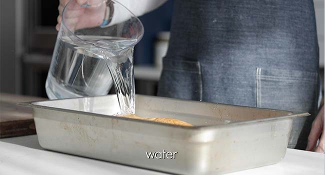 pouring water over bread in a large pan