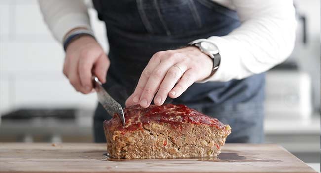 slicing glazed cooked meatloaf on a cutting board