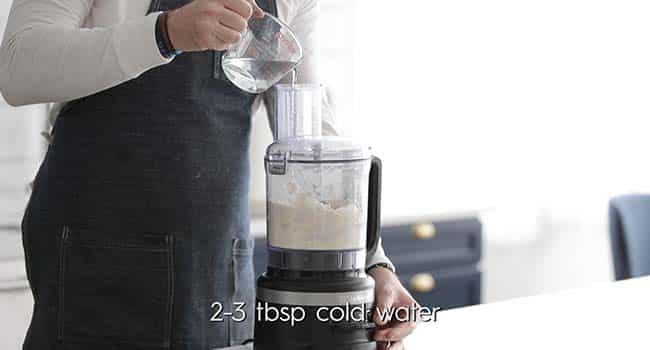adding water to a food processor with flour while pulsing