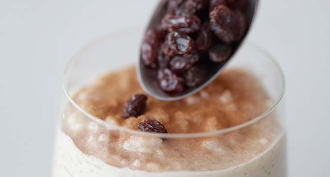 adding raisins to a glass with rice pudding and cinnamon