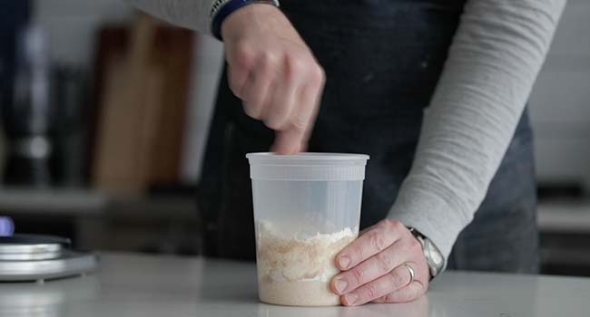 mixing together a sourdough starter in a plastic container