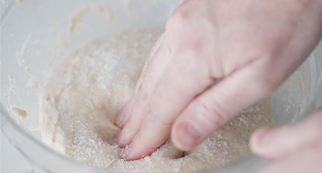 mixing in sea salt to sourdough bread dough in a bowl