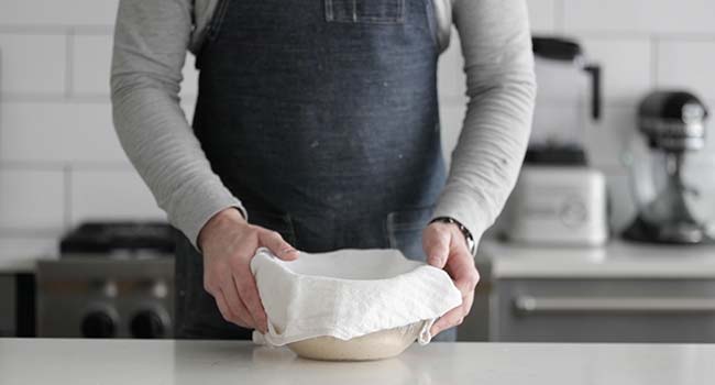 bowl of sourdough bread dough covered with a towel