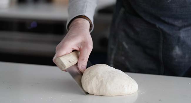 forming bread dough on a countertop with a bench knife