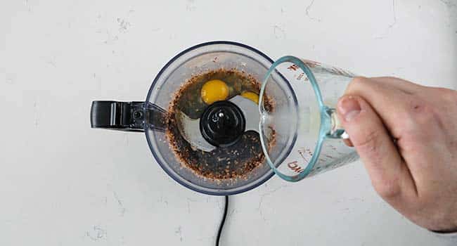 adding eggs and lemon juice to a food processor with anchovies and garlic
