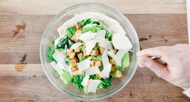 adding dressing to a bowl with greens and cheese