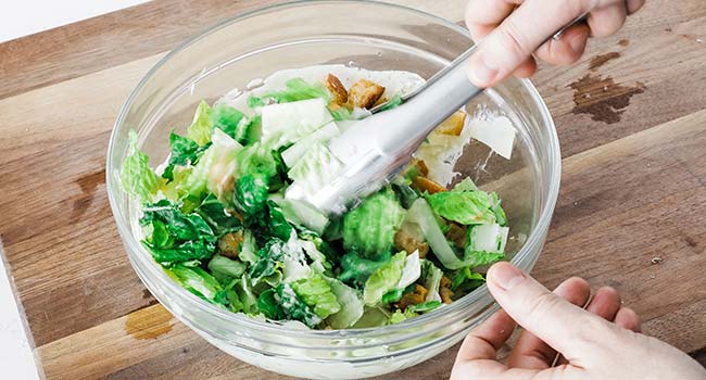 mixing a caesar salad together in a bowl