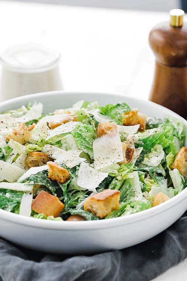 a caesar salad with dressing and parmesan cheese shavings