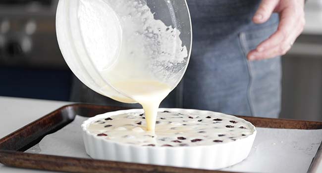 pouring batter from a bowl into a tart pan with cherries