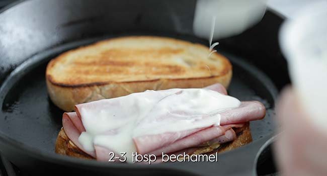 bechamel sauce being poured over ham slices on toast