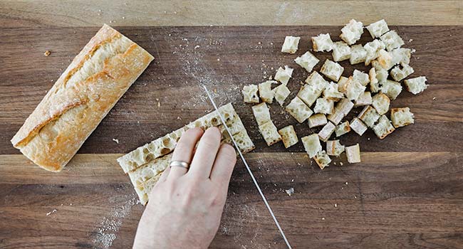 cutting a baguette into small bite-size pieces on a cutting board