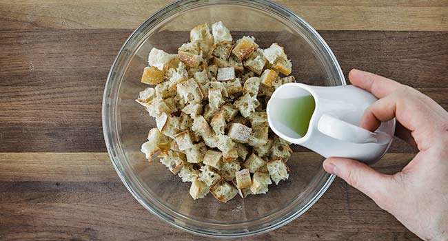 adding olive oil to a bowl full of small cubed bread
