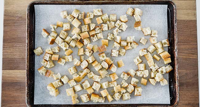 croutons spread out on a cookie sheet tray with parchment paper