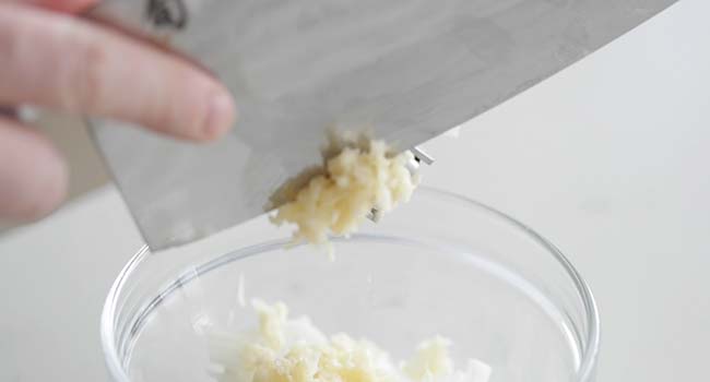 adding chopped garlic to a bowl