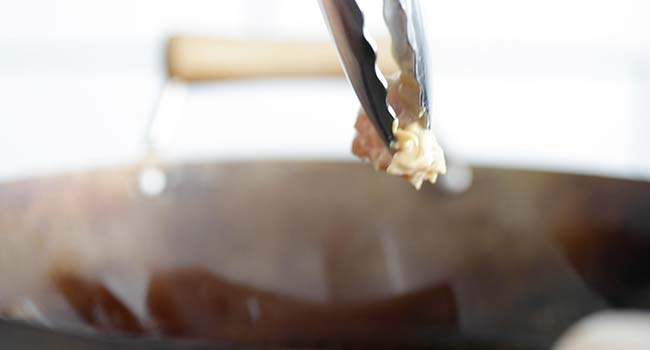 adding flour breaded chicken to a wok