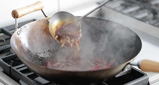 stirring a sauce with onions in a wok